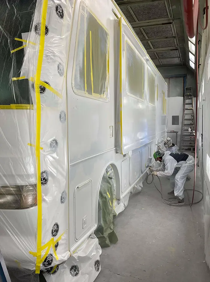 Photo of a recreational vehicle in a paint booth receiving a layer of primer before the paint job is started.